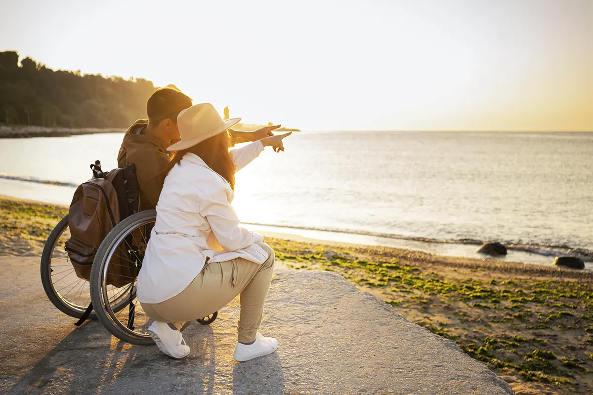 un hombre en silla de ruedas contemplando una puesta de sol junto a su pareja