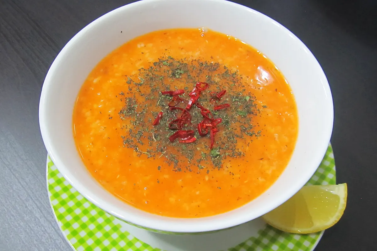 Un cuenco blanco sobre un plato verde que contiene sopa de Ezogelin