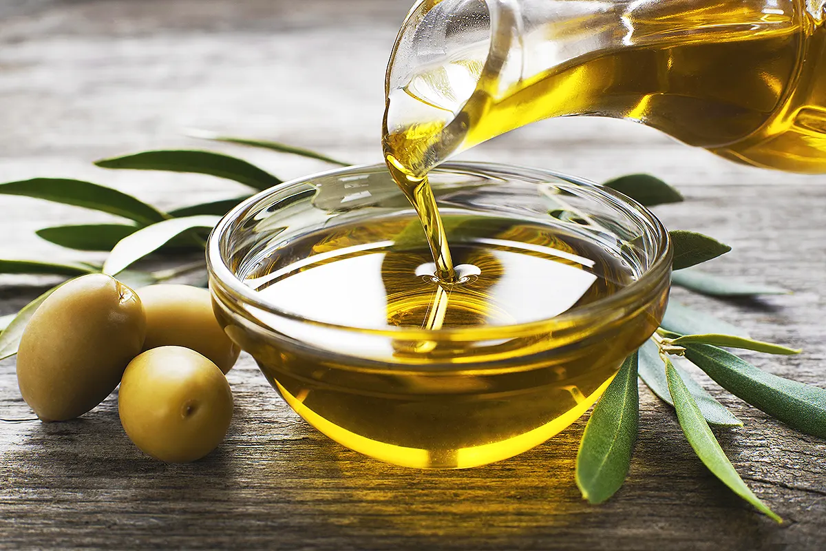 un cuenco con aceite de oliva junto a unas aceitunas sobre una mesa