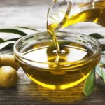 a bowl with olive oil next to some olives on a table