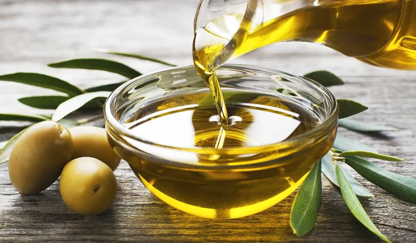 a bowl with olive oil next to some olives on a table