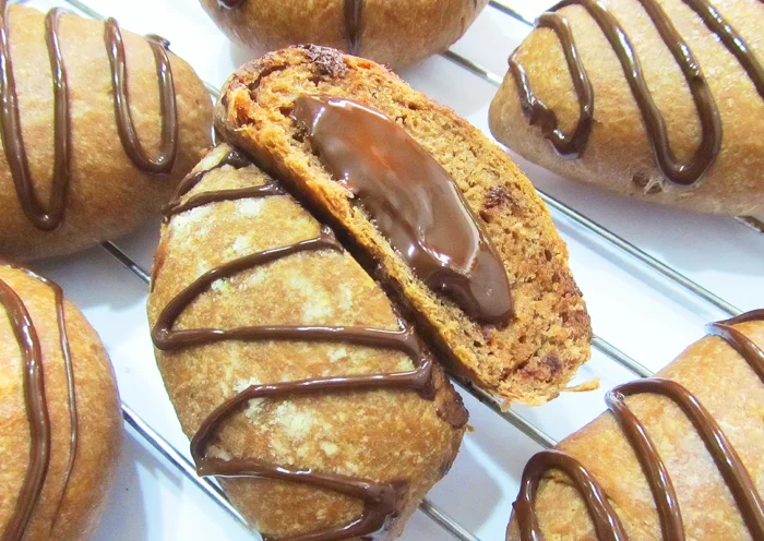 several buns made with flour and cocoa and decorated, one of them split and showing its chocolate filling inside