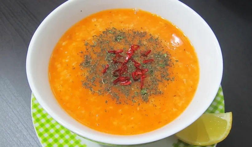 A white bowl on a green plate containing Ezogelin soup.