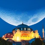 The Grand Hagia Sophia Mosque in Istanbul during the holy month of Ramadan is illuminated at night with a huge waning moon in the background.