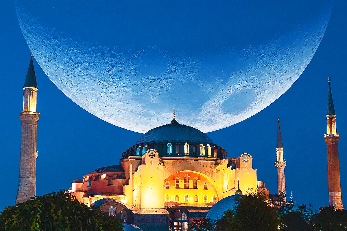 The Grand Hagia Sophia Mosque in Istanbul during the holy month of Ramadan is illuminated at night with a huge waning moon in the background.