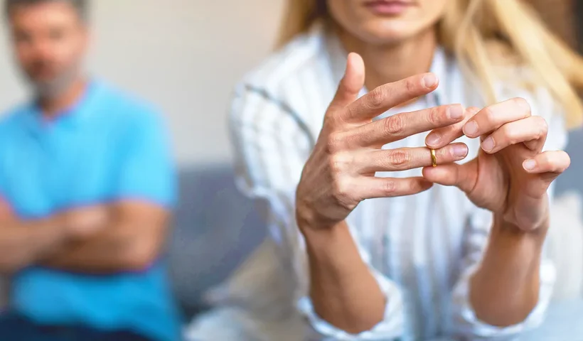 un matrimonio con una mujer joven y rubia en primer plano quitándose el anillo de casados, y de fondo el marido mirándola
