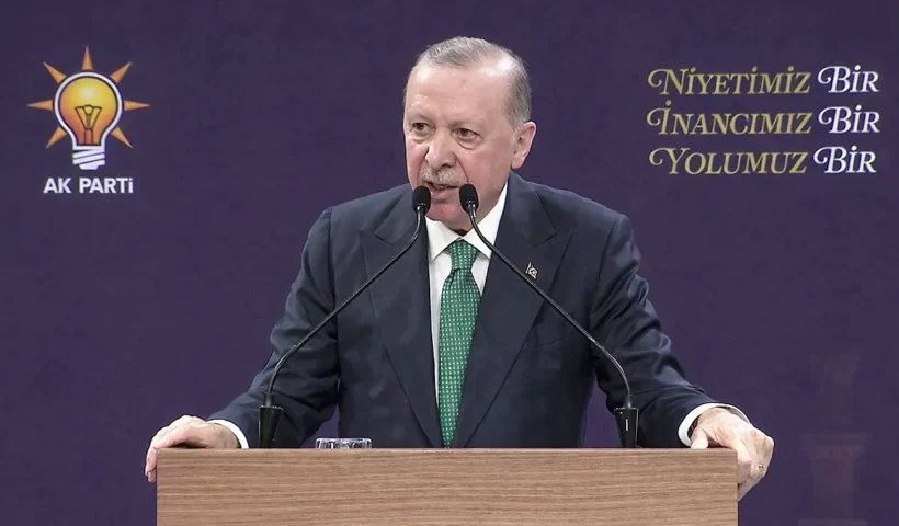 Turkish President Tayyip Erdoğan speaks from a pulpit with an AKP party symbol in the background.