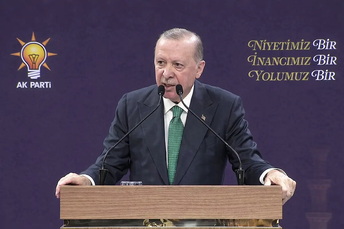 Turkish President Tayyip Erdoğan speaks from a pulpit with an AKP party symbol in the background.