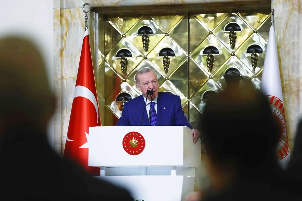 el presidente turco Tayyip Erdoğan pronuncia un discurso ante una audiencia desde un podio, junto a una bandera de Turquía
