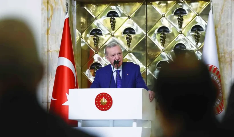 Turkish President Tayyip Erdoğan addresses an audience from a podium, next to a Turkish flag.