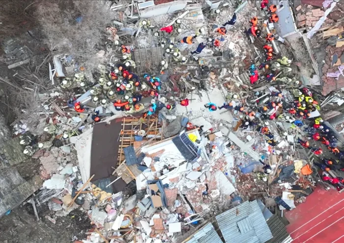 dozens of rescue team members seen from the air as they work over an area between several buildings devastated by an explosion