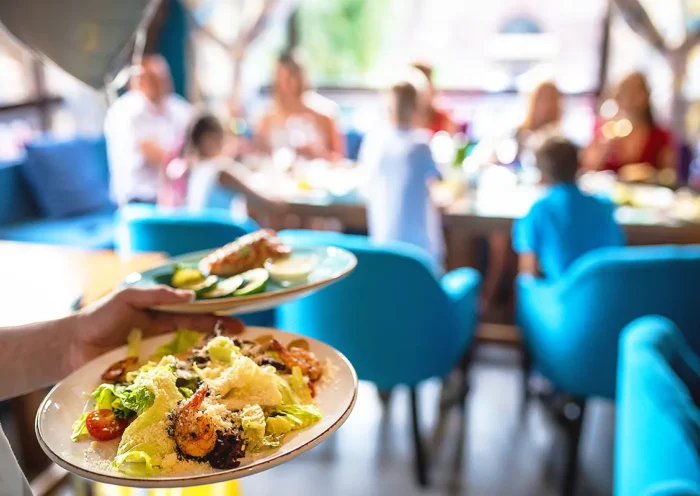 a waiter serving two plates of food with salad and seafood to a table where there is a family with several children