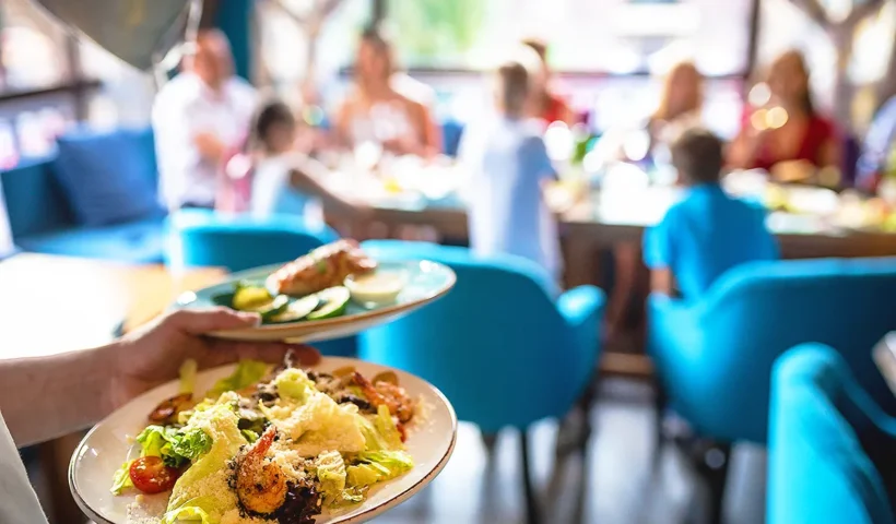 a waiter serving two plates of food with salad and seafood to a table where there is a family with several children