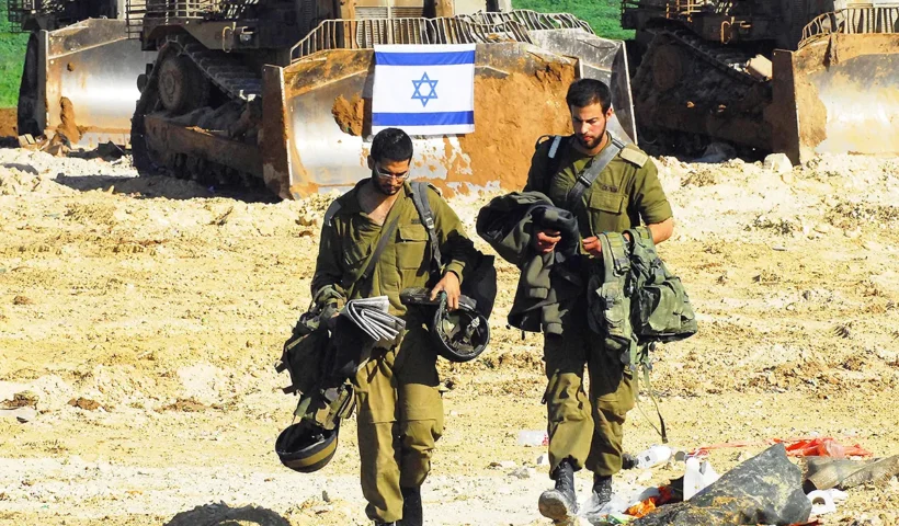 dos soldados israelíes caminan desprovistos de parte de su equipamiento, detrás de ellos dos bulldozers y una bandera de Israel