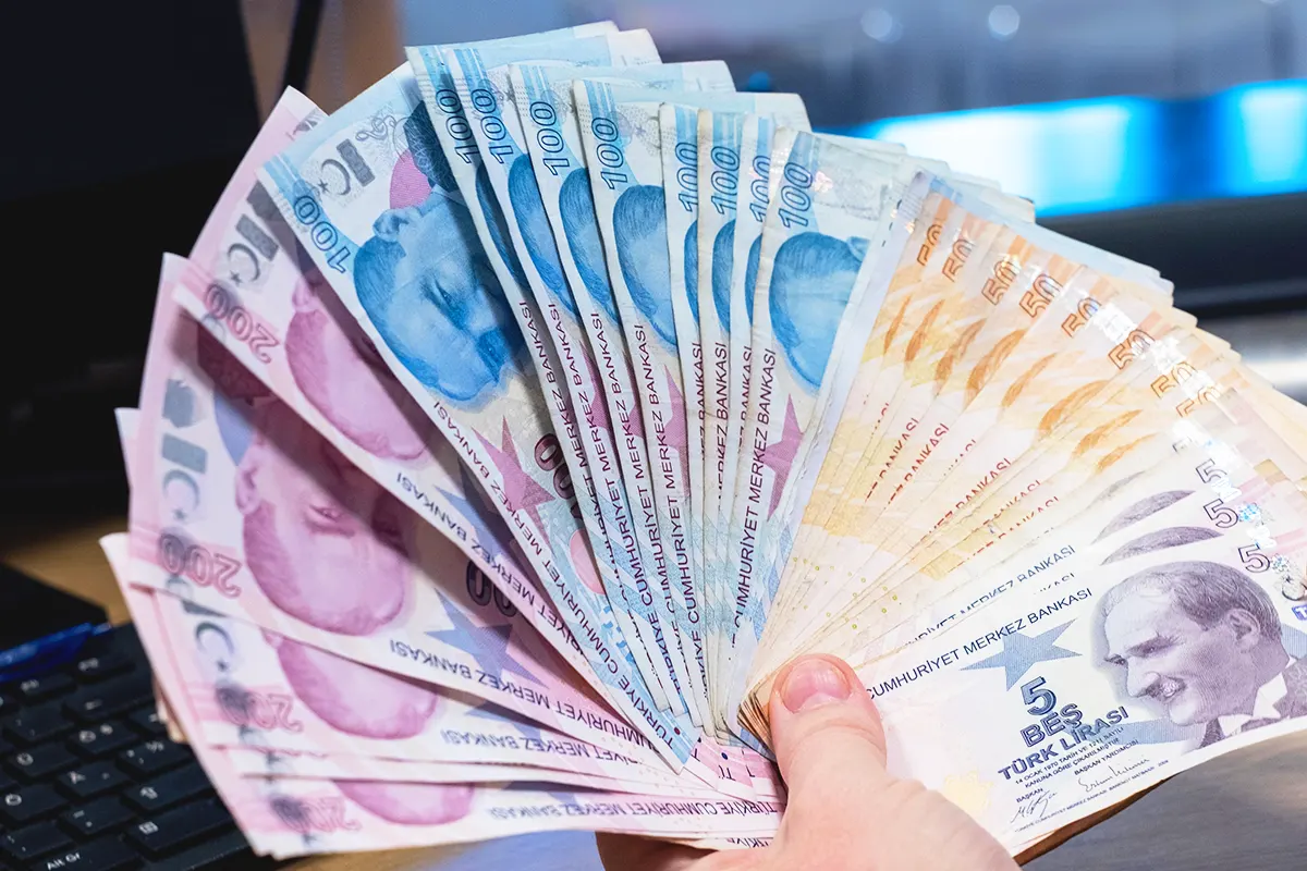 a hand holds a wad of Turkish lira banknotes in a fanned out position