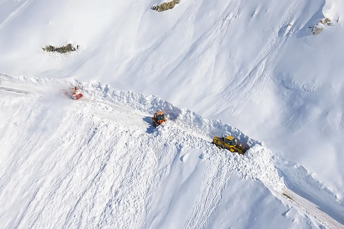varias máquinas quitanieves vistas desde el aire avanzando a través de una carretera de montaña totalmente cubierta por las nevadas