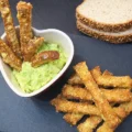 on a blackboard several cheese coated crispbread sticks, some slices of bread, and a heart-shaped bowl where several sticks are dipped in avocado sauce