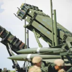 two Patriot missile defence batteries together next to two soldiers
