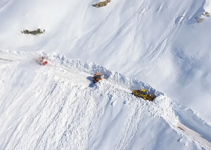several snow ploughs seen from the air moving along a mountain road completely covered by snowfall