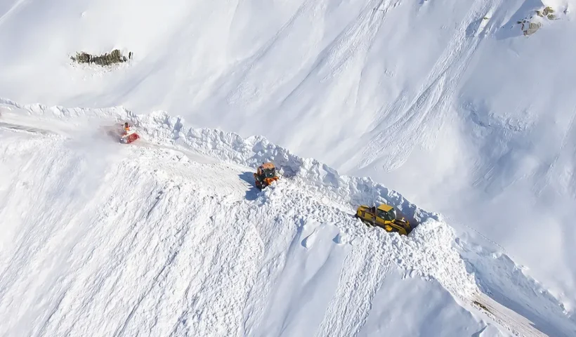 several snow ploughs seen from the air moving along a mountain road completely covered by snowfall
