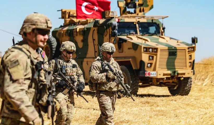 soldados estadounidenses armados caminan junto a un vehículo blindado militar con la bandera de Turquía en un campo de Irak