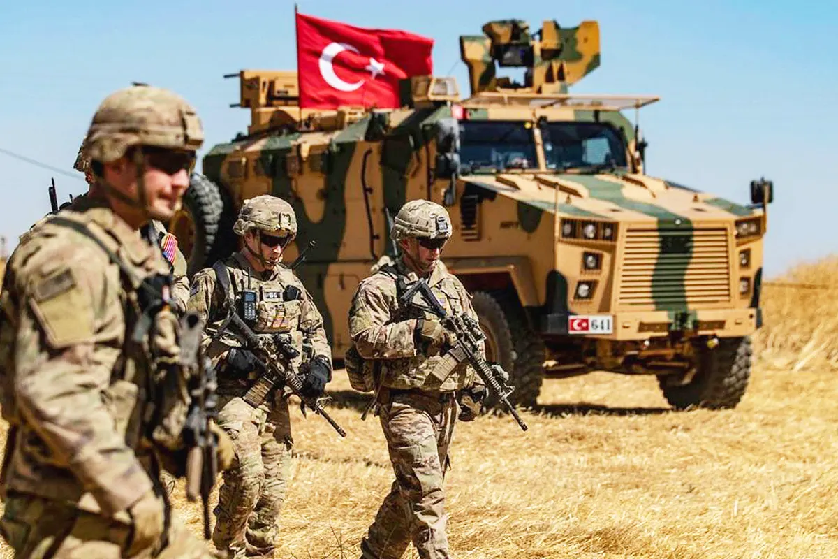 soldados estadounidenses armados caminan junto a un vehículo blindado militar con la bandera de Turquía en un campo de Irak