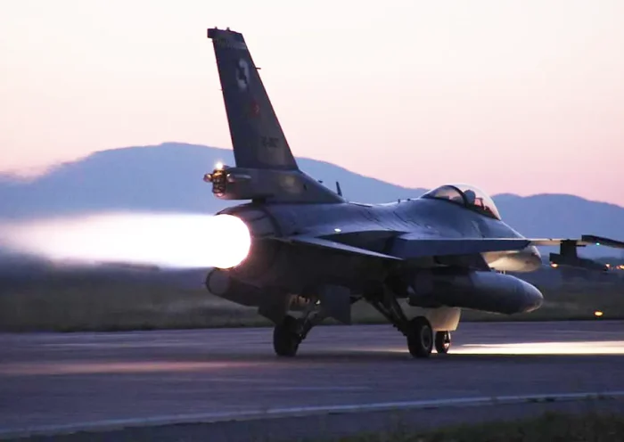 A Turkish army F-16 fighter jet taking off in the twilight with its jet engine at full power.