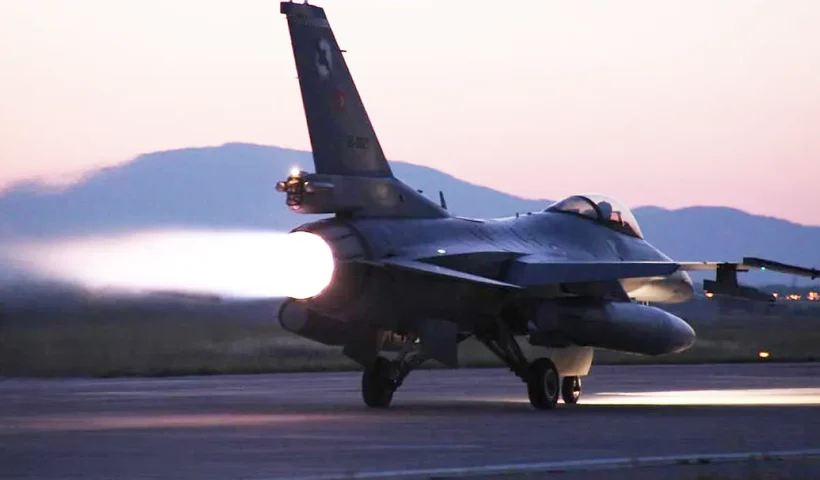 A Turkish army F-16 fighter jet taking off in the twilight with its jet engine at full power.