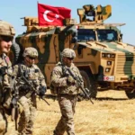 Armed US soldiers walk past a military armoured vehicle with the Turkish flag in a field in Iraq.