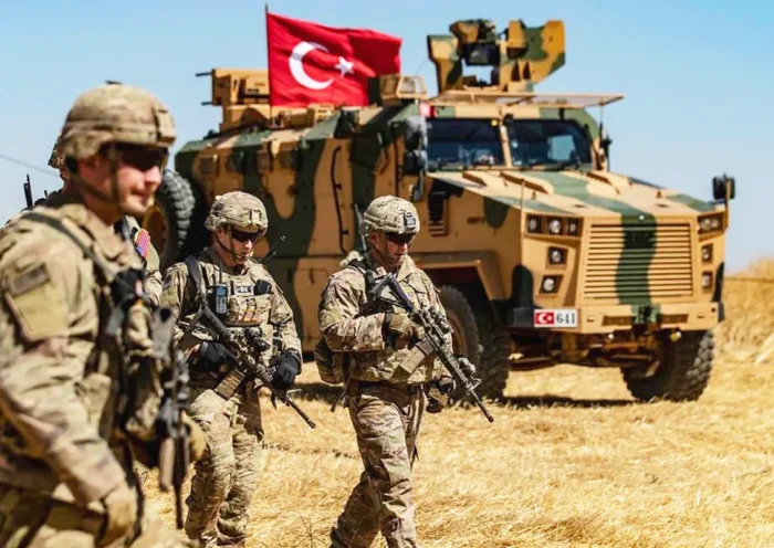 Armed US soldiers walk past a military armoured vehicle with the Turkish flag in a field in Iraq.