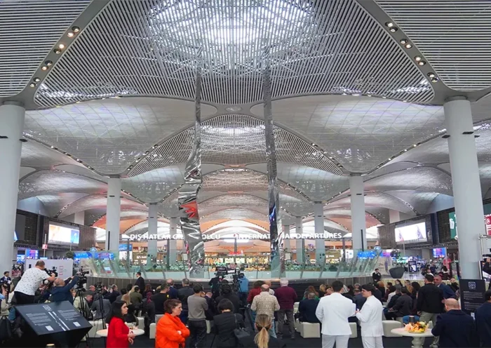 a picture of a giant sculpture consisting of two vertical metal pieces, surrounded by people inside Istanbul Airport
