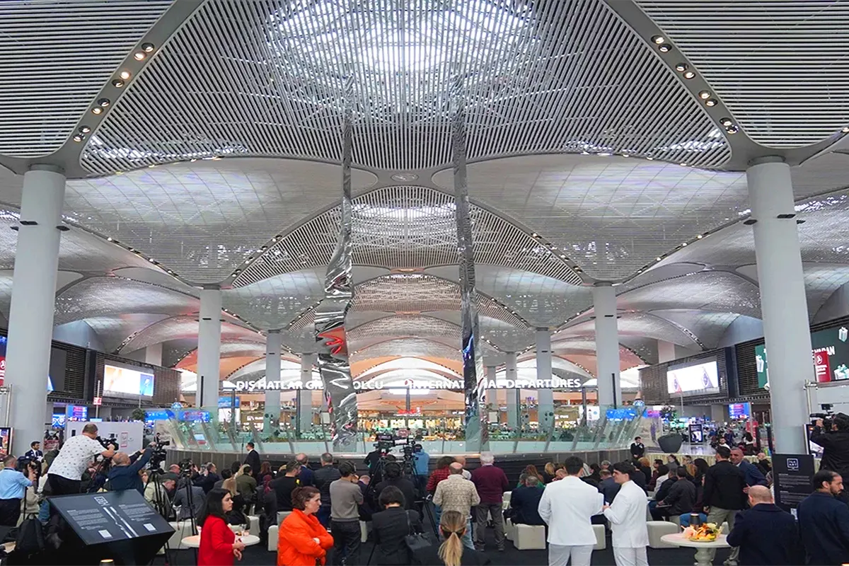 a picture of a giant sculpture consisting of two vertical metal pieces, surrounded by people inside Istanbul Airport
