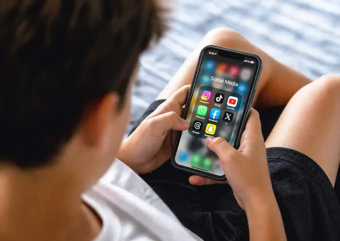 A child sits looking at a mobile phone screen displaying various social media icons