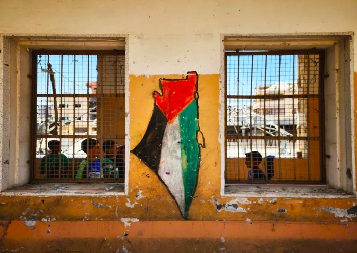 some Palestinian children inside a ruined house with railings in the West Bank, on the front of which a Palestinian flag has been painted