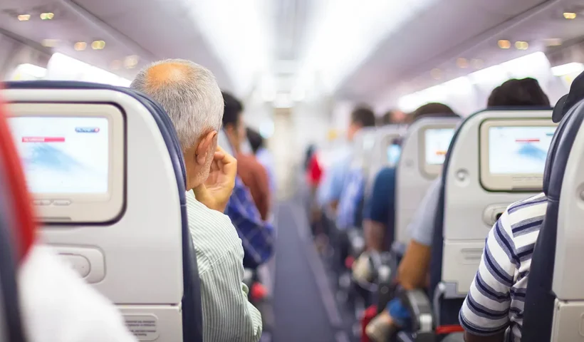 A view of the aisle in an aeroplane cabin, with several passengers sitting with their backs to the camera.