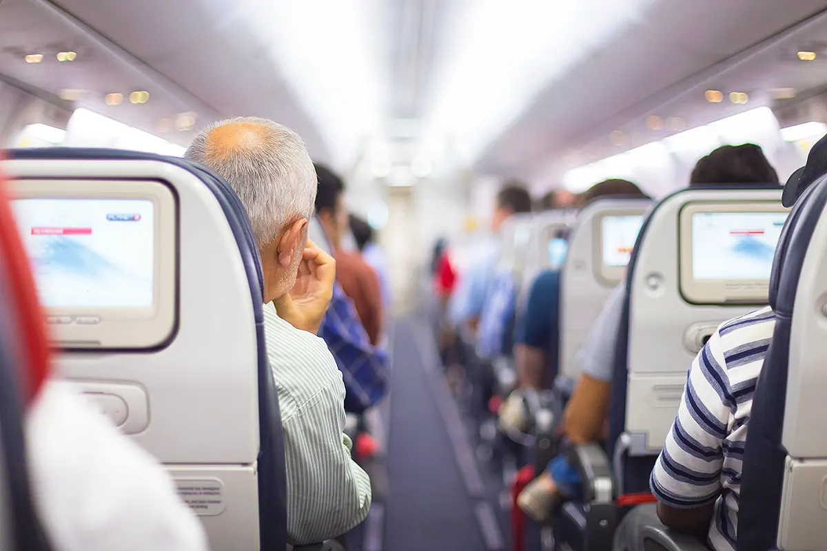 A view of the aisle in an aeroplane cabin, with several passengers sitting with their backs to the camera.
