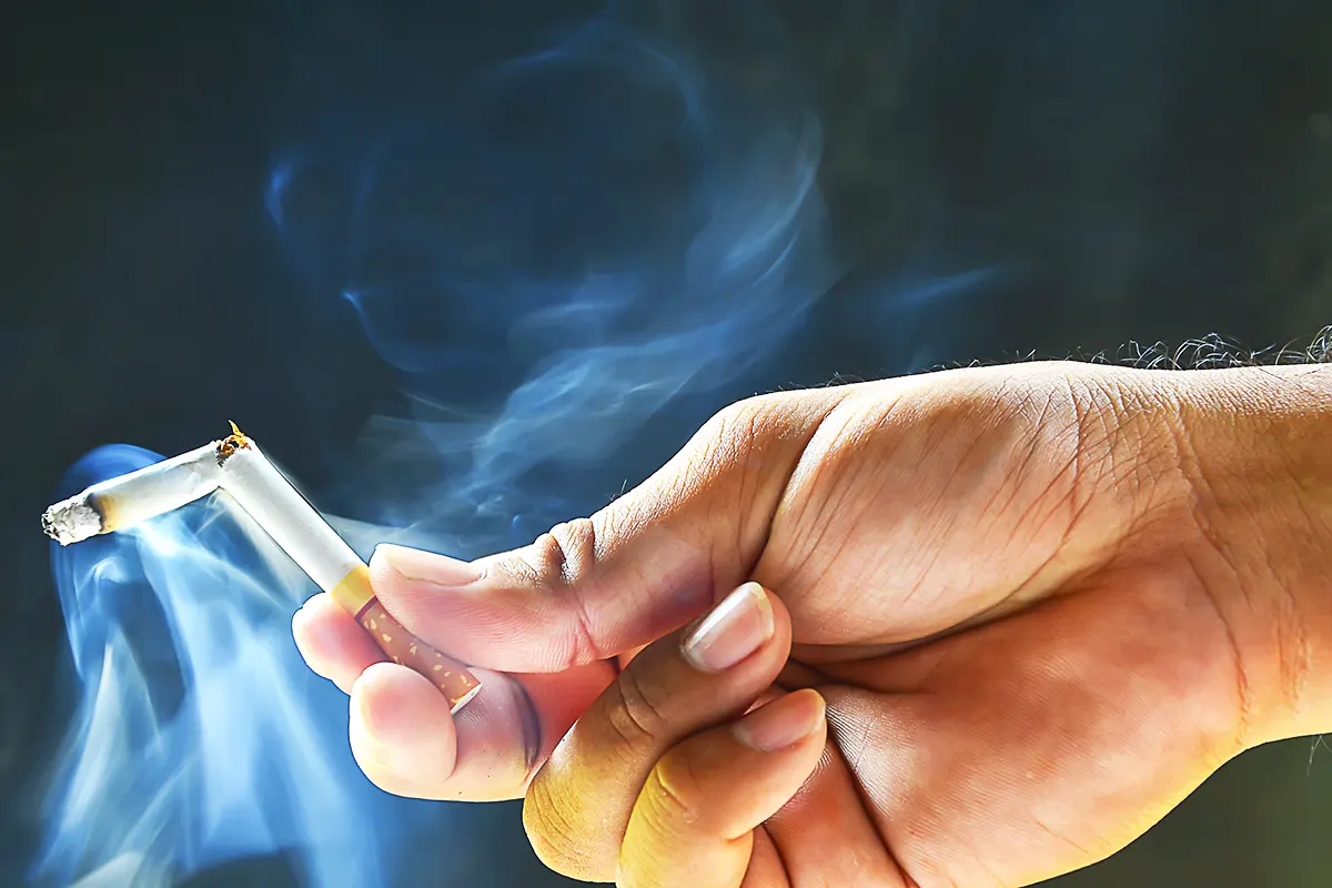 una mano sostiene un cigarrillo humeante partido por la mitad