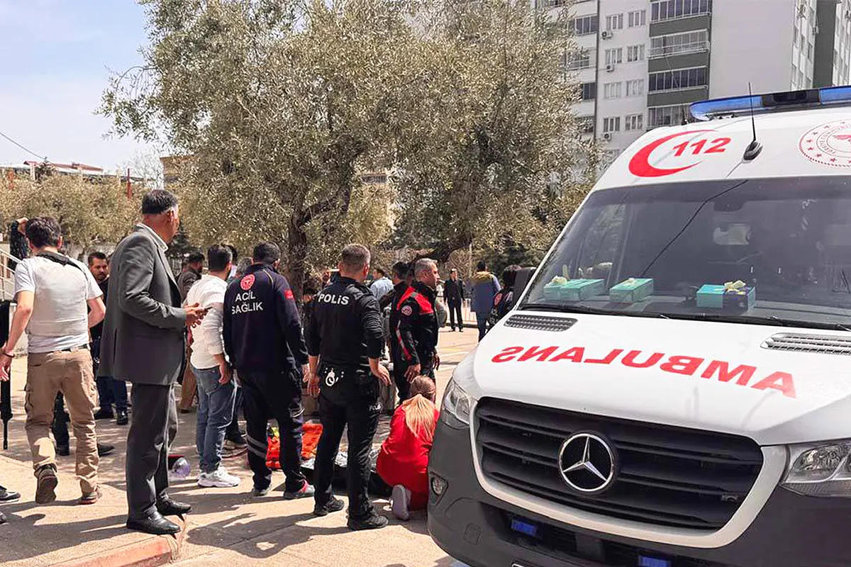 Several people standing next to an ambulance and a victim lying on the ground outside a school in Turkey