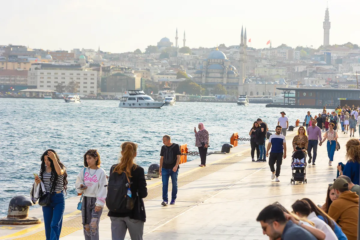 gente paseando junto al mar en el estuario del Cuerno de Oro de Estambul, con varios edificios históricos y mezquitas al fondo