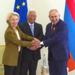 Armenian Prime Minister Pashinyan shakes hands with António Costa and Ursula von der Leyen next to an EU flag and an Armenian flag.