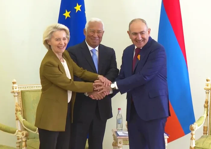 Armenian Prime Minister Pashinyan shakes hands with António Costa and Ursula von der Leyen next to an EU flag and an Armenian flag.