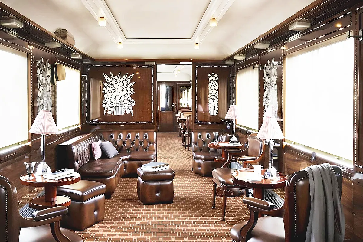 interior de un vagón del Orient Express mostrando un salón decorado lujosamente con muebles de madera, decoraciones de cristal y sillones de piel