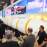 un enorme misil balístico colocado de forma horizontal se muestra durante una feria llena de gente, incluyendo militares