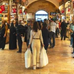 una mujer en primer plano cargando con bolsas con compras atravesando el interior del Bazar Egipcio de Estambul, lleno de tiendas y de gente