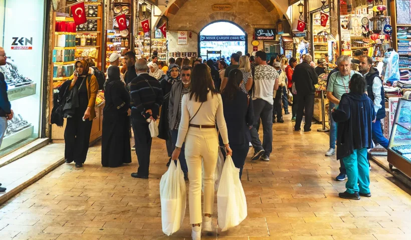 una mujer en primer plano cargando con bolsas con compras atravesando el interior del Bazar Egipcio de Estambul, lleno de tiendas y de gente