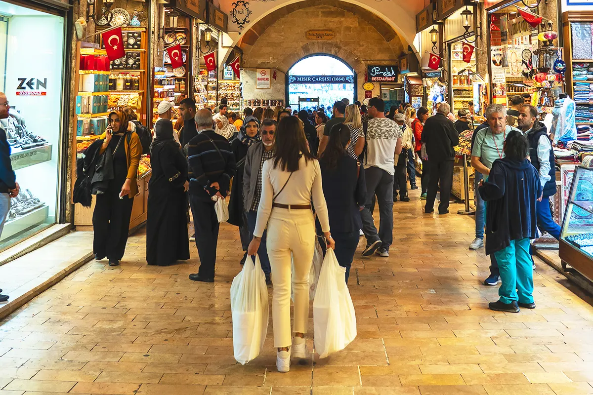 una mujer en primer plano cargando con bolsas con compras atravesando el interior del Bazar Egipcio de Estambul, lleno de tiendas y de gente