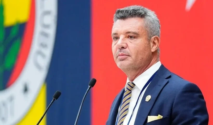 el presidente del Fenerbahçe, Sadettin Saran, aparece en primer plano hablando por dos micrófonos; de fondo se ve un enorme escudo del Fenerbahçe