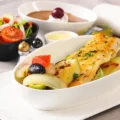 a Turkish Airlines in-flight menu showing, in the foreground, a plate of fish alongside a bowl of salad, a cream dessert and a rolled-up napkin