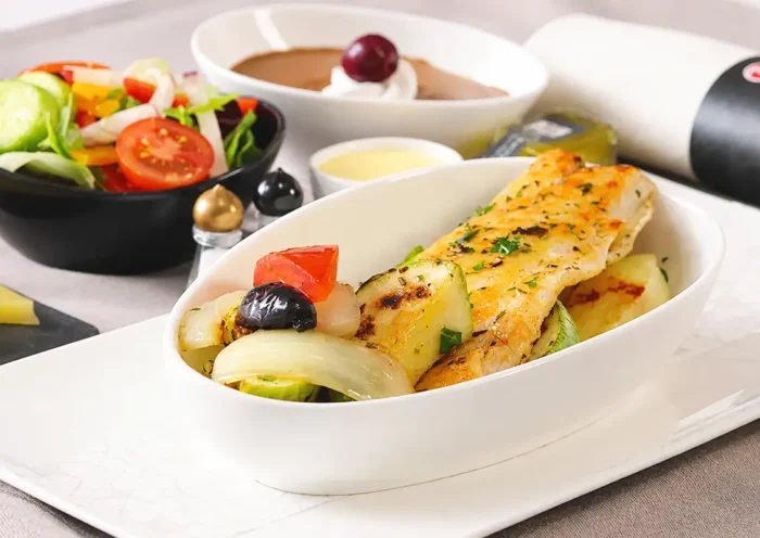 a Turkish Airlines in-flight menu showing, in the foreground, a plate of fish alongside a bowl of salad, a cream dessert and a rolled-up napkin