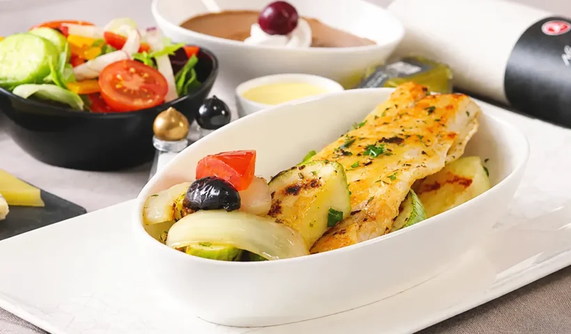 a Turkish Airlines in-flight menu showing, in the foreground, a plate of fish alongside a bowl of salad, a cream dessert and a rolled-up napkin